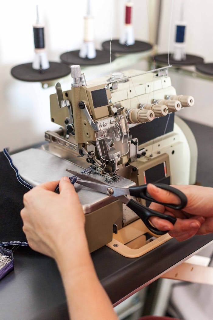 Close-up of hands cutting fabric near a sewing machine, illustrating textile work.